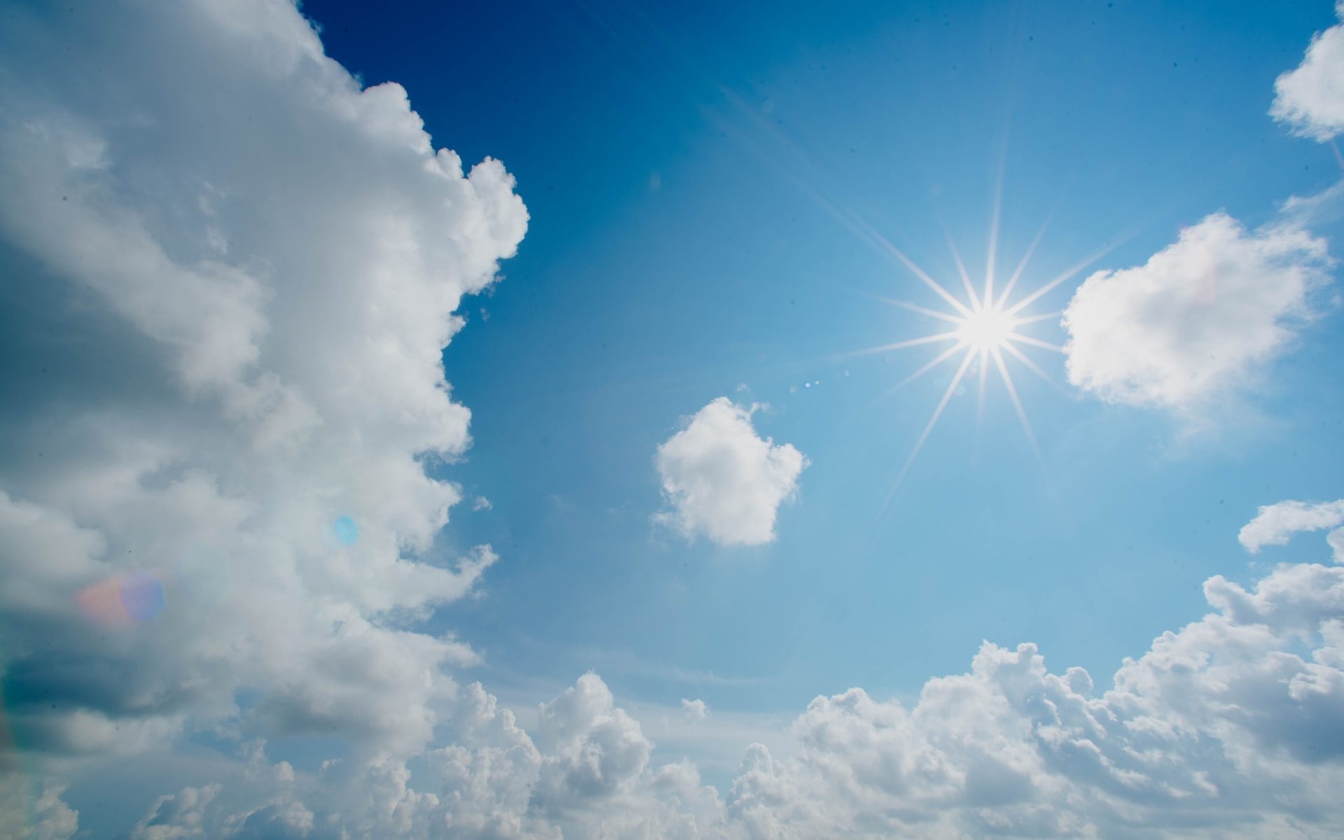 Sun shining in a blue sky with white clouds