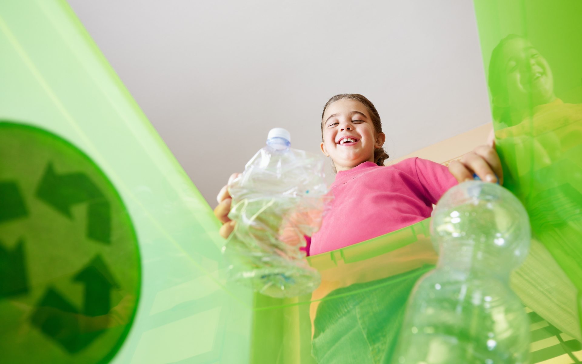 A young girl placing plastic bottles into a recycling bin