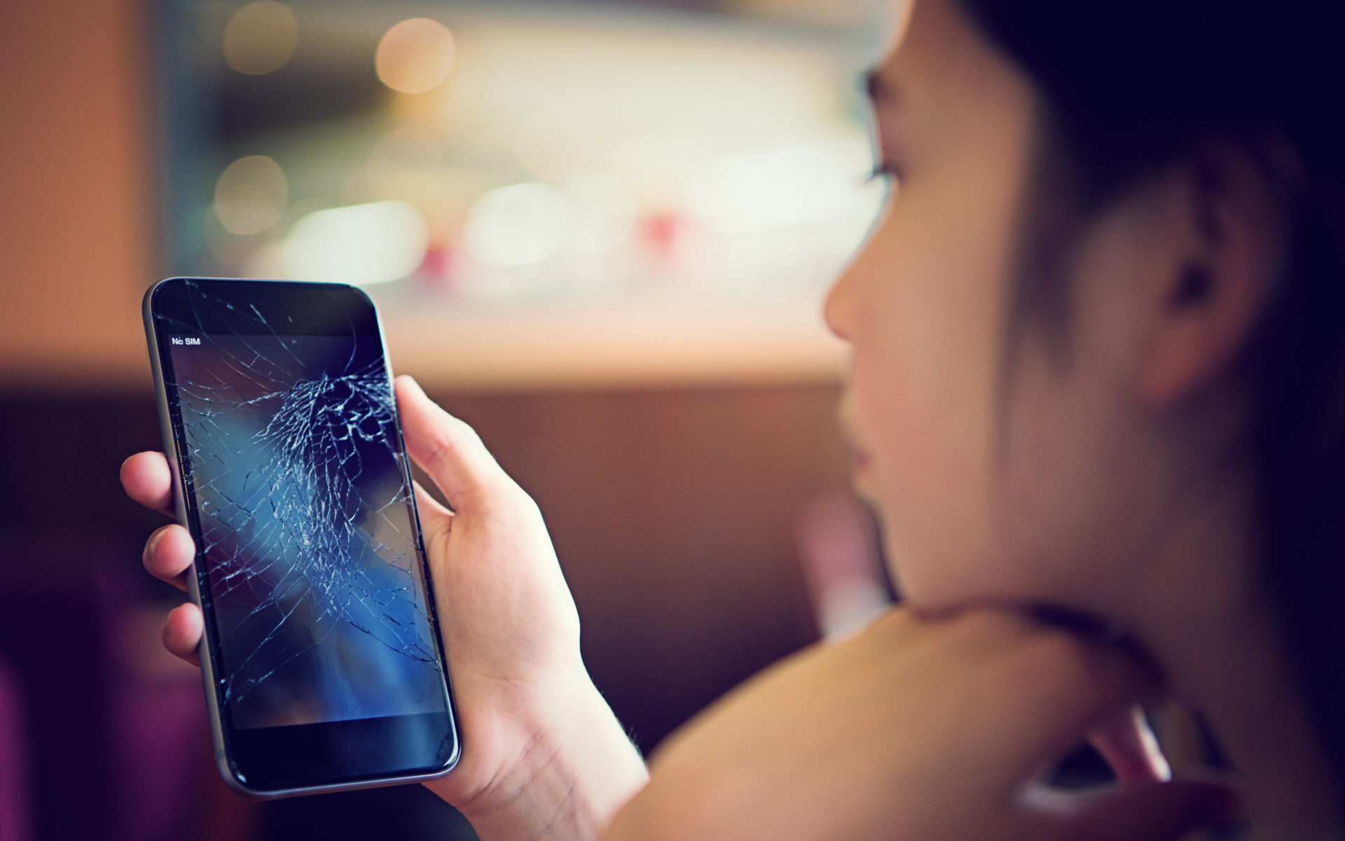 A young woman looking sadly at her broken smartphone